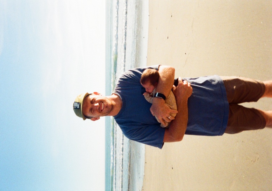 Price on the beach holding a newborn